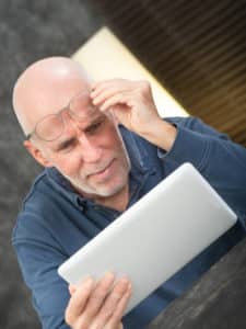 Senior man using a tablet, he is having difficulties and vision problems