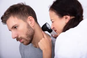 Close-up Of A Young Female Doctor Checking Skin On Man's Neck With Dermatoscope