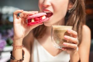 Happy asian woman tasting delicious macaroon in cafe. Breakfast and french cuisine concept