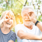 Seniors in the park with happy face smiling doing ok sign with hand on eye looking through fingers.