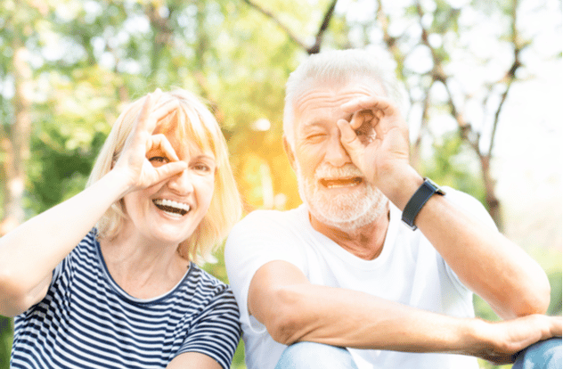 Seniors in the park with happy face smiling doing ok sign with hand on eye looking through fingers.