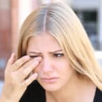 A woman with allergic eyelid problems rubbing her eye